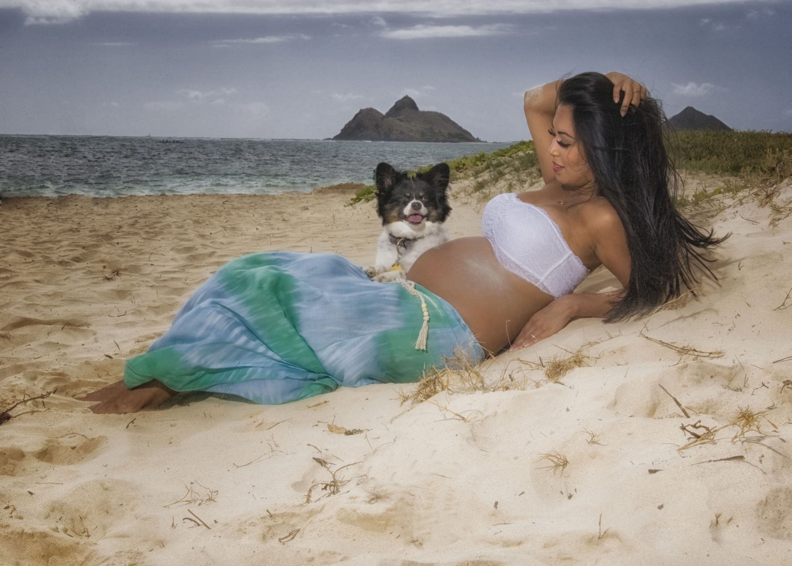 Pregnant woman relaxing on beach with dog.