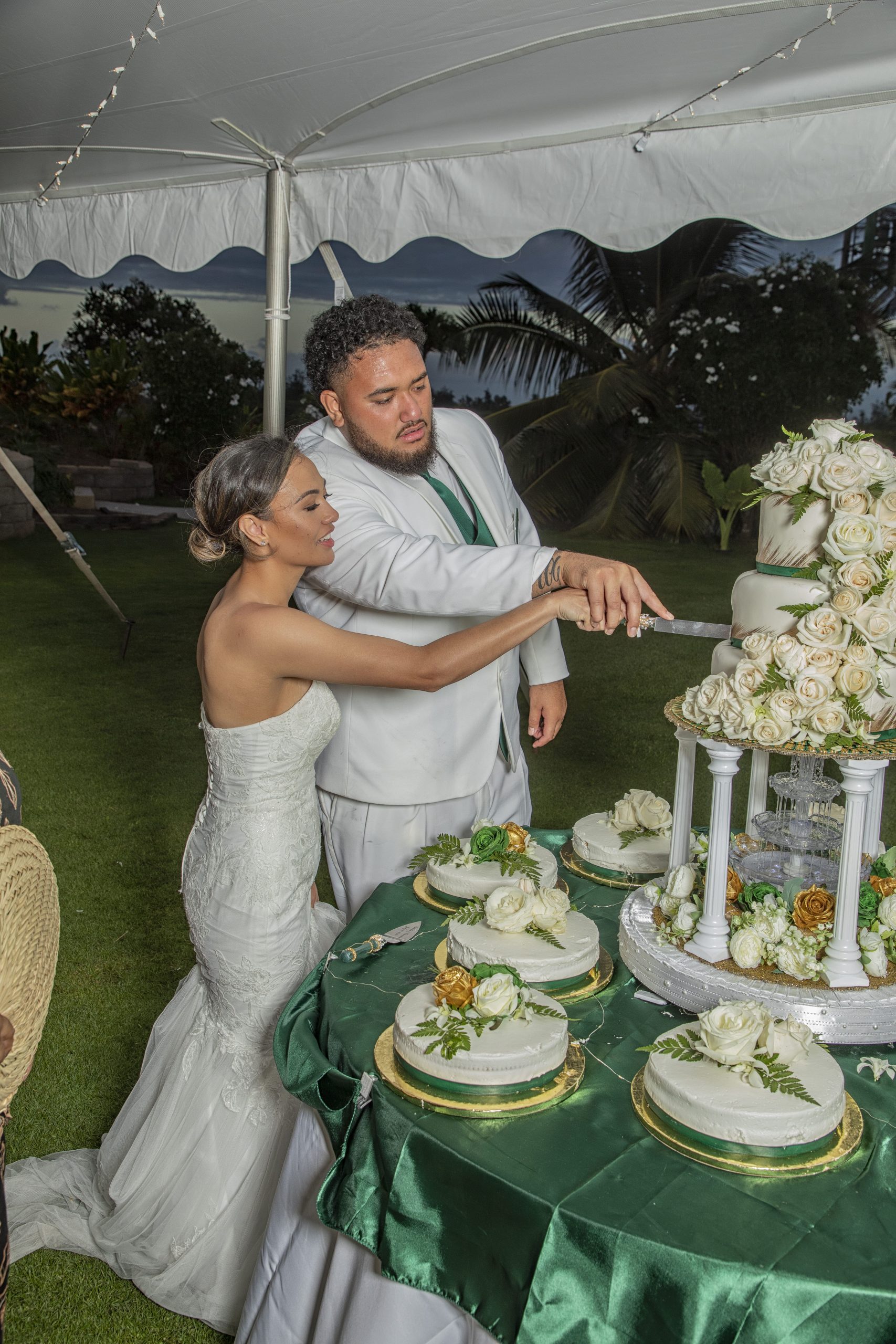 Couple cutting wedding cake outdoors under tent.