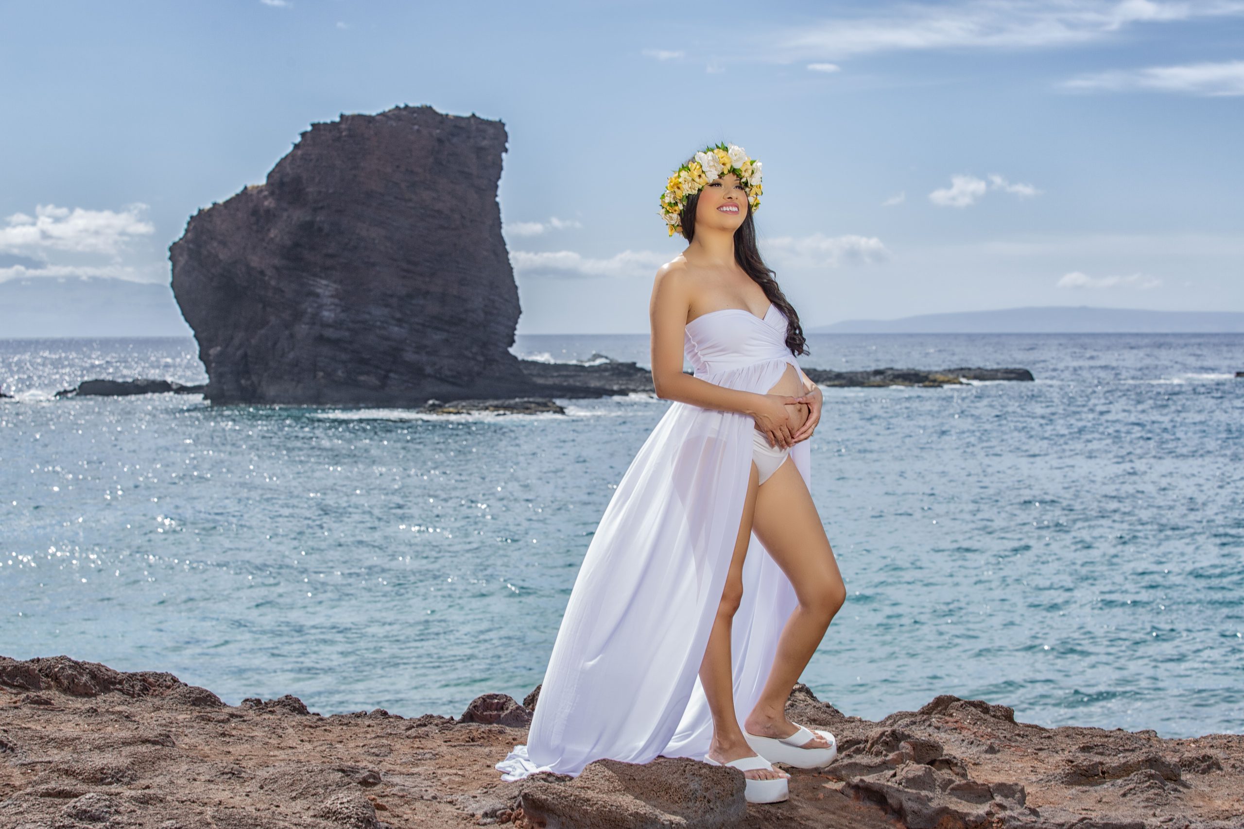 Pregnant woman in a white dress by the ocean.
